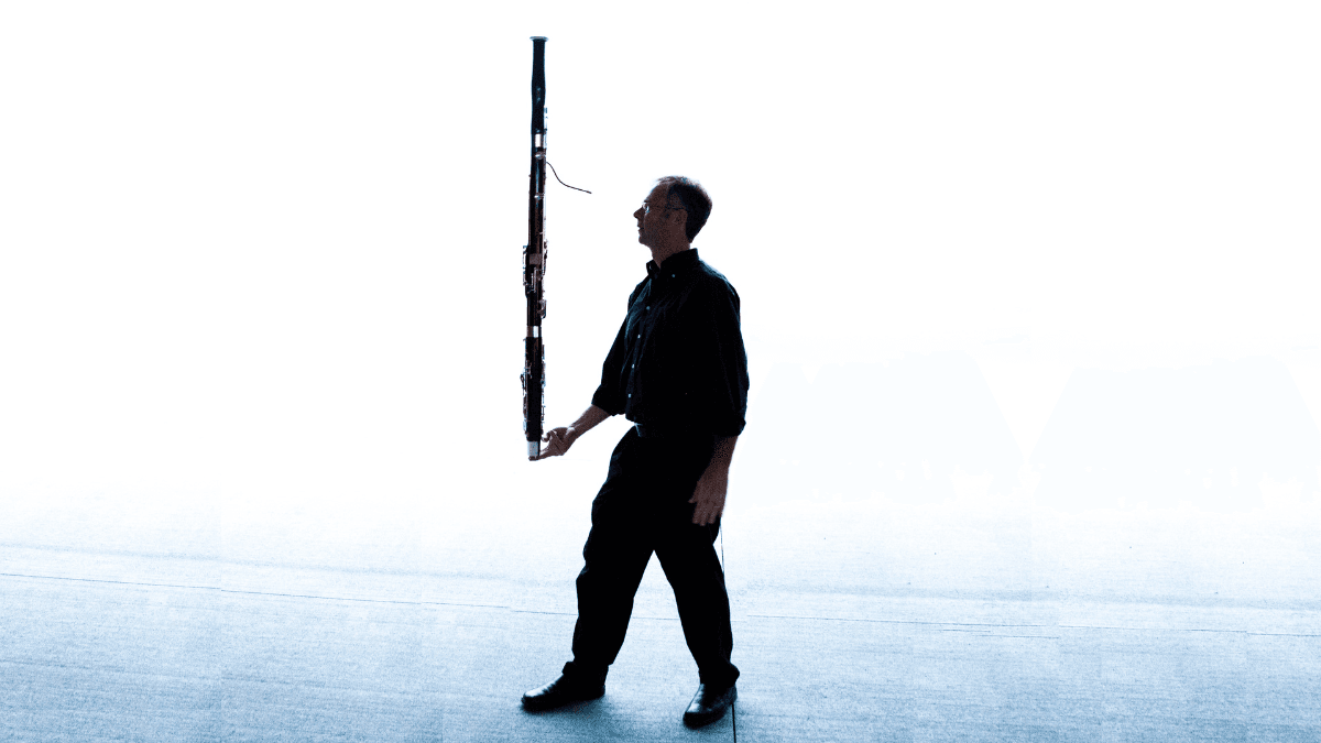 A silhouetted image of bassoon professor Doug Spaniol balancing his instrument on one hand against a bright background.