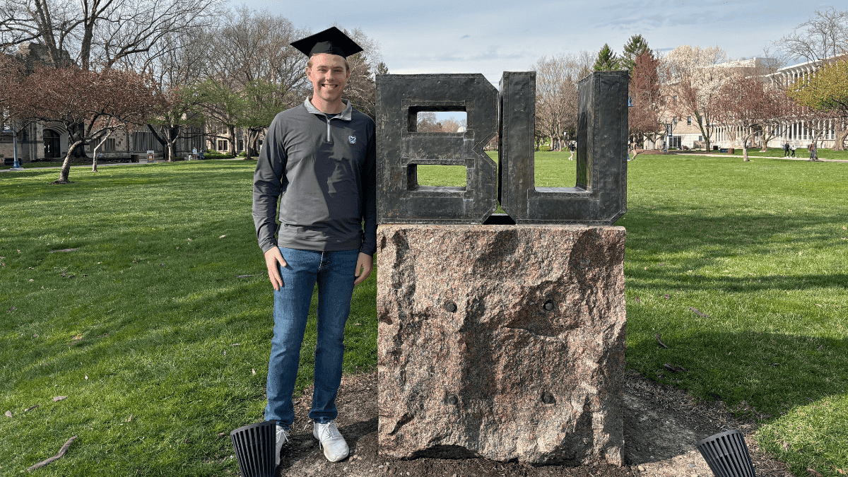 Butler 2024 graduate Tristan Rumsey stands near the BU statue on the mall wearing his graduation cap.